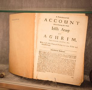 An old book displayed on a shelf, open to a page titled “Account of the Routing the whole Irish Army at Aghrim,” features aged, yellowed pages and printed text recounting the historic Battle of Aughrim.